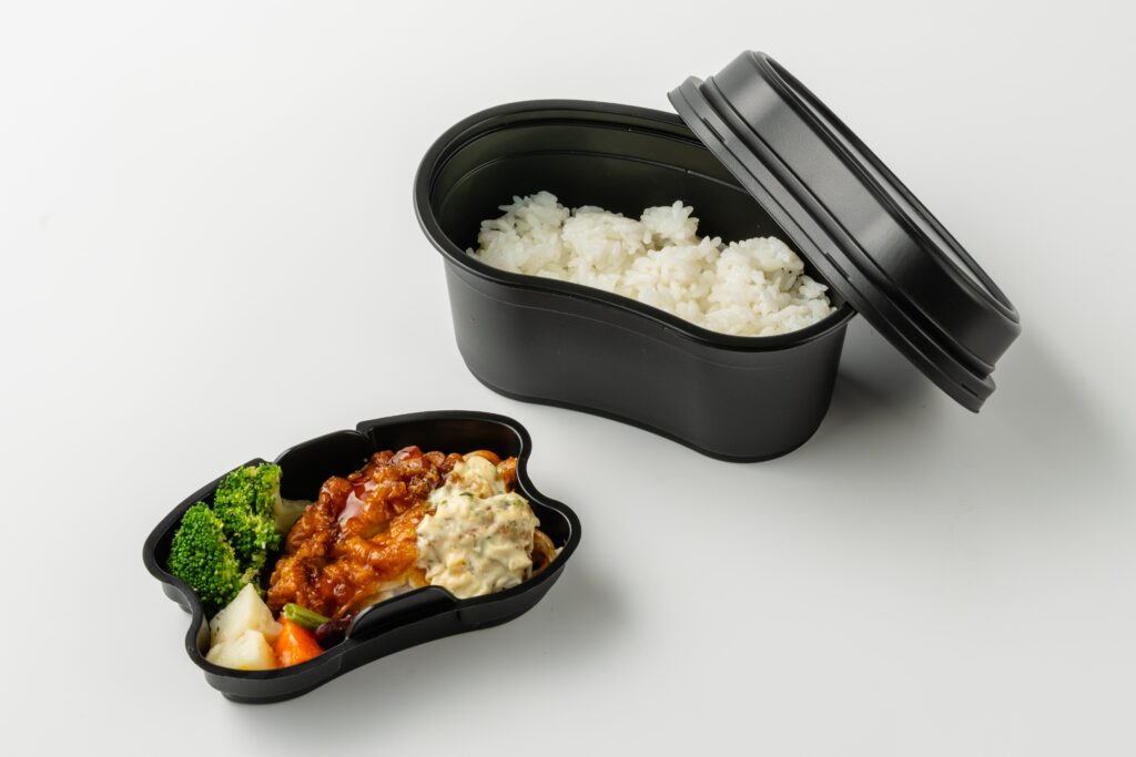「飯ごう」モチーフのテイクアウト容器にご飯と惣菜を盛りつけたイメージ